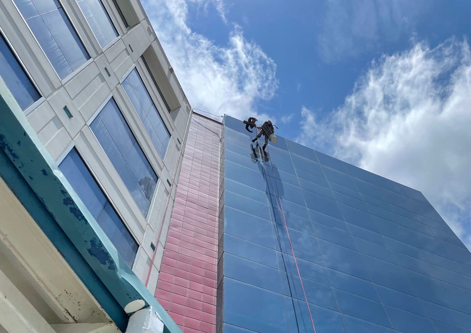 Rope-access technician inspecting and cleaning a high-rise glass facade